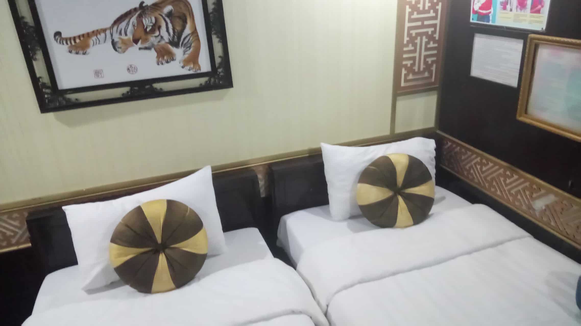 My Halong Bay Cruise Experience in Vietnam 7 Cabin on our Halong Bay cruise in Vietnam with two twin beds next to one another, each with two pillows, and a tiger painting on the wall behind
