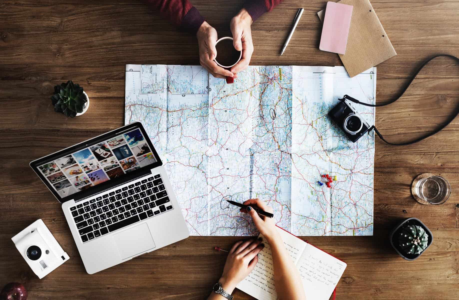 Two people sit across a table from one another with a map in between them, planning a trip