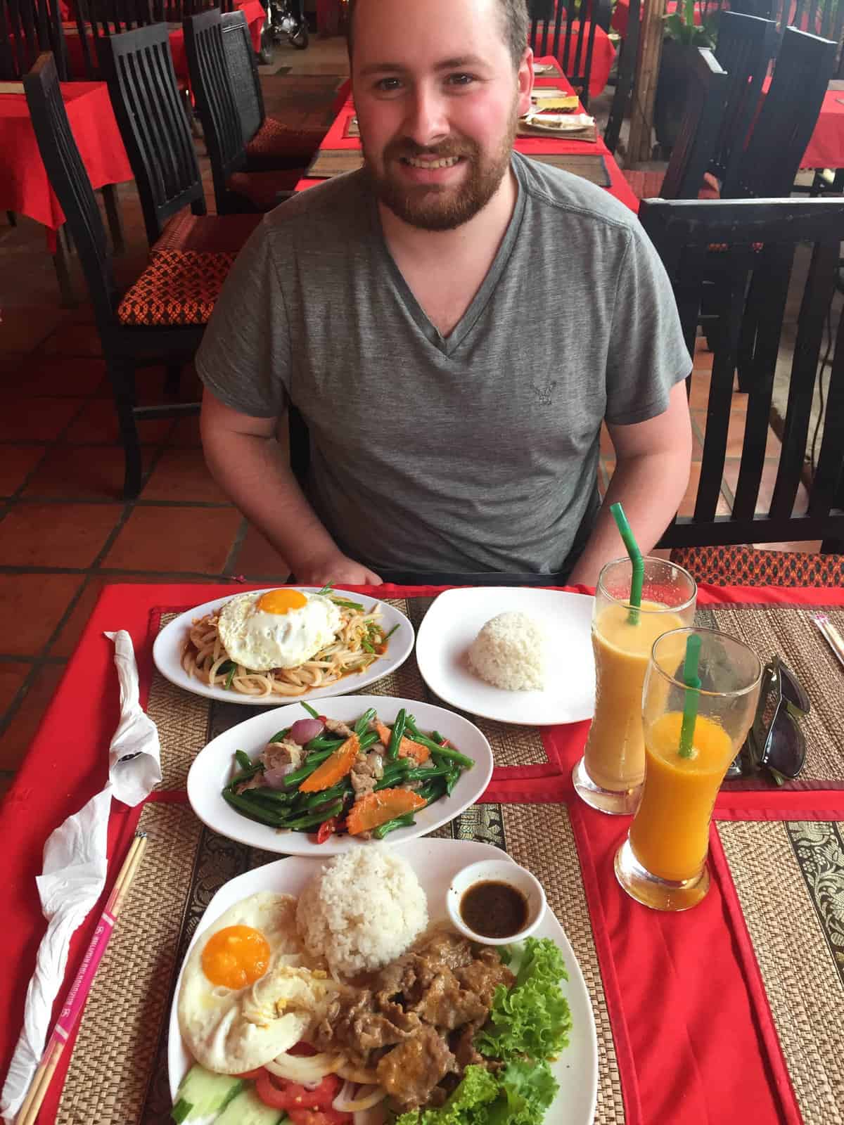 The Best and Worst of Southeast Asia 8 Colin sitting at a table in Siem Reap, Cambodia showing off a whole table of food and two drinks