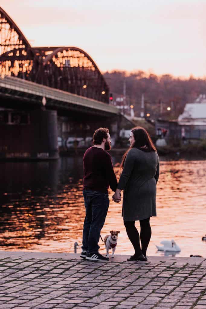 Expat Reflections: 6 Months of Living in Prague 6 Colin and Riana standing on the riverfront holding hands and looking out with their dog Ellie on the ground between them; Family Photos in Prague