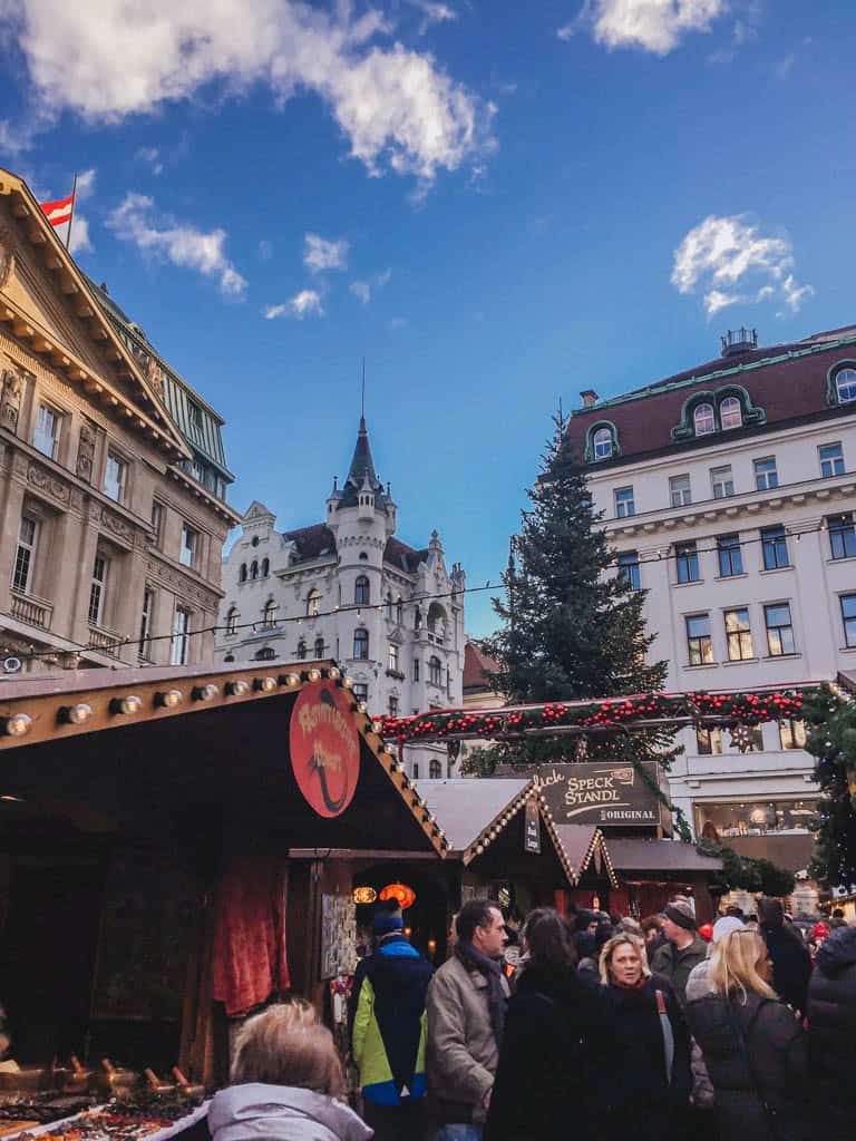 The Ultimate European Christmas Market Road Trip 18 Christmas market in Vienna with crowds at stalls and beautiful buildings in the background