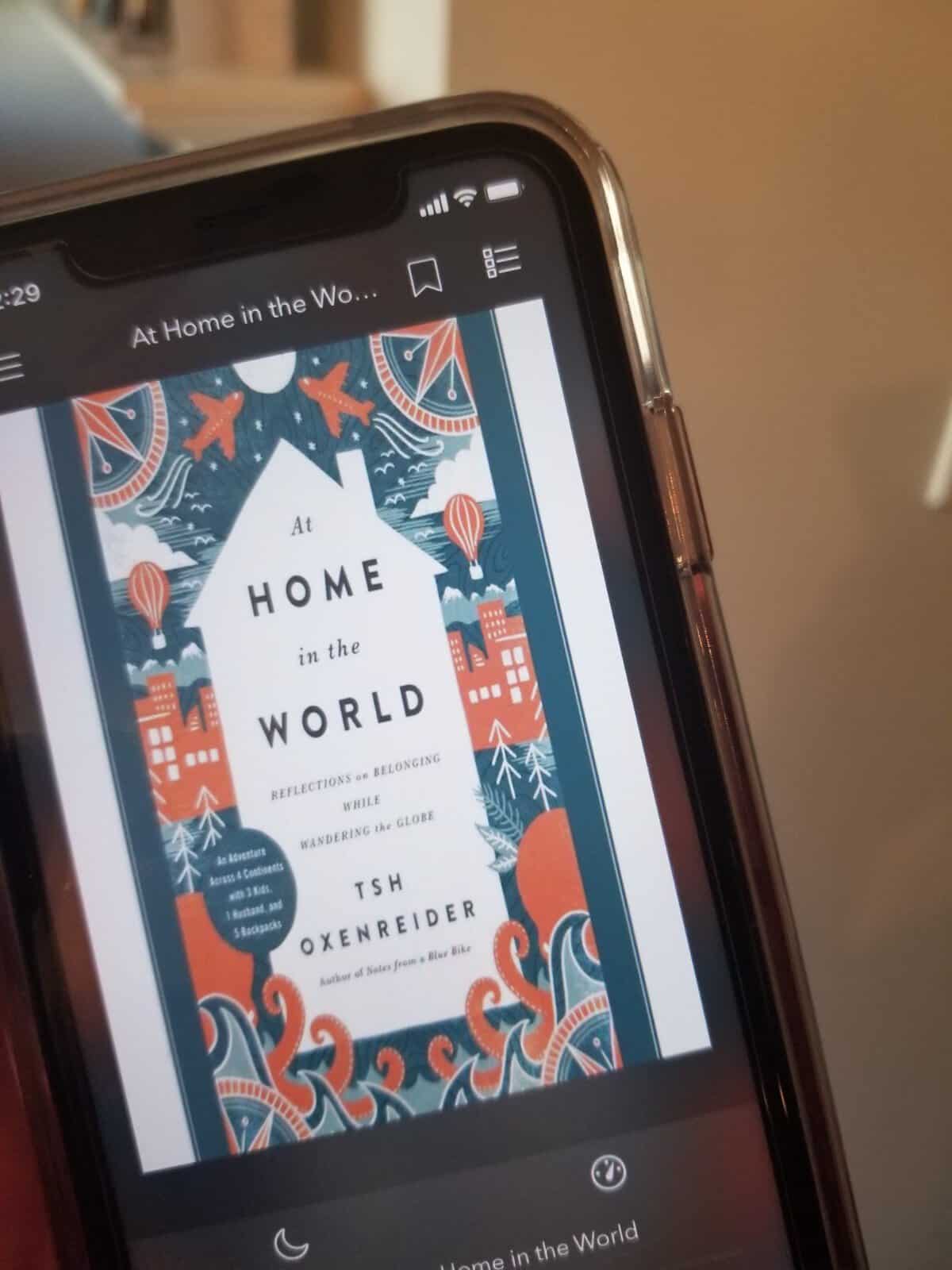 40+ Beach Reads for Every Reading Mood 4 Riana holding her iPhone where the screen shows she's listening to the audiobook of At Home in the World