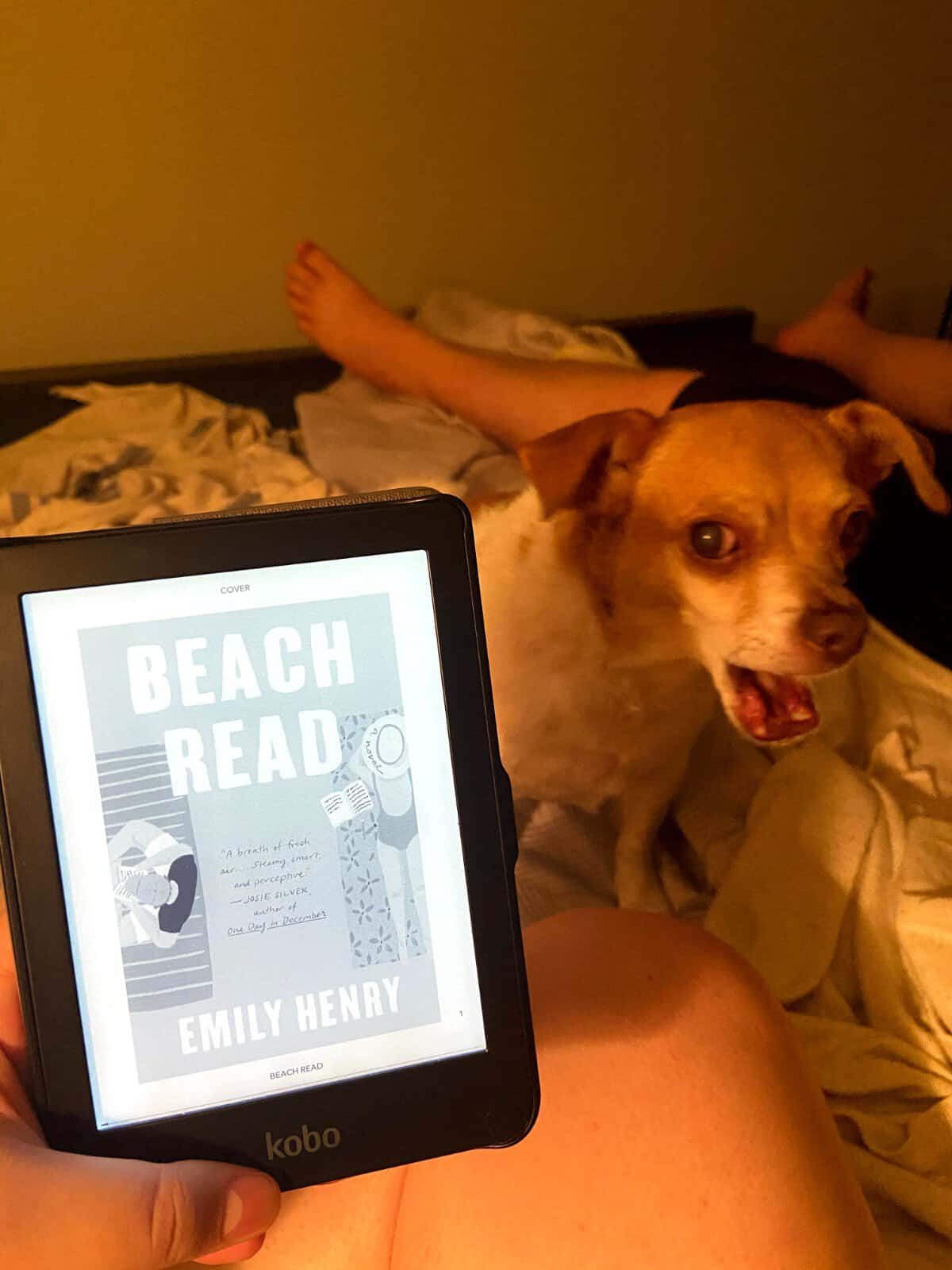 40+ Beach Reads for Every Reading Mood 11 Holding the ebook of Beach Read by Emily Henry with my dog Ellie in the background