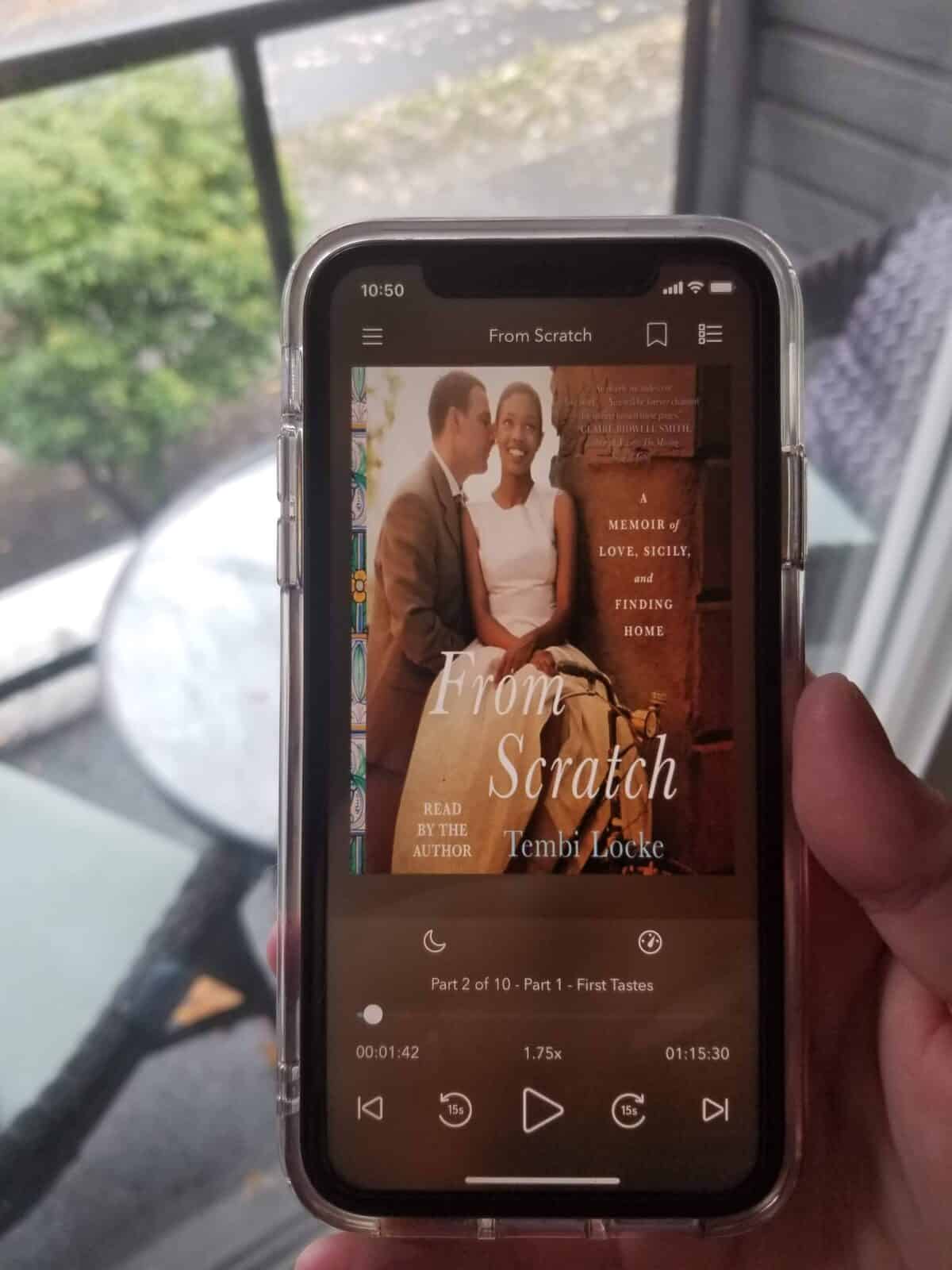 40+ Beach Reads for Every Reading Mood 7 Riana holding her iPhone where the screen shows she's listening to the audiobook of From Scratch
