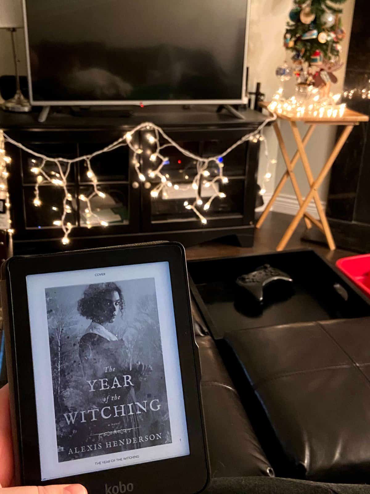 40+ Beach Reads for Every Reading Mood 21 Ebook of The Year of the Witching by Alexis Henderson with Christmas lights in the background