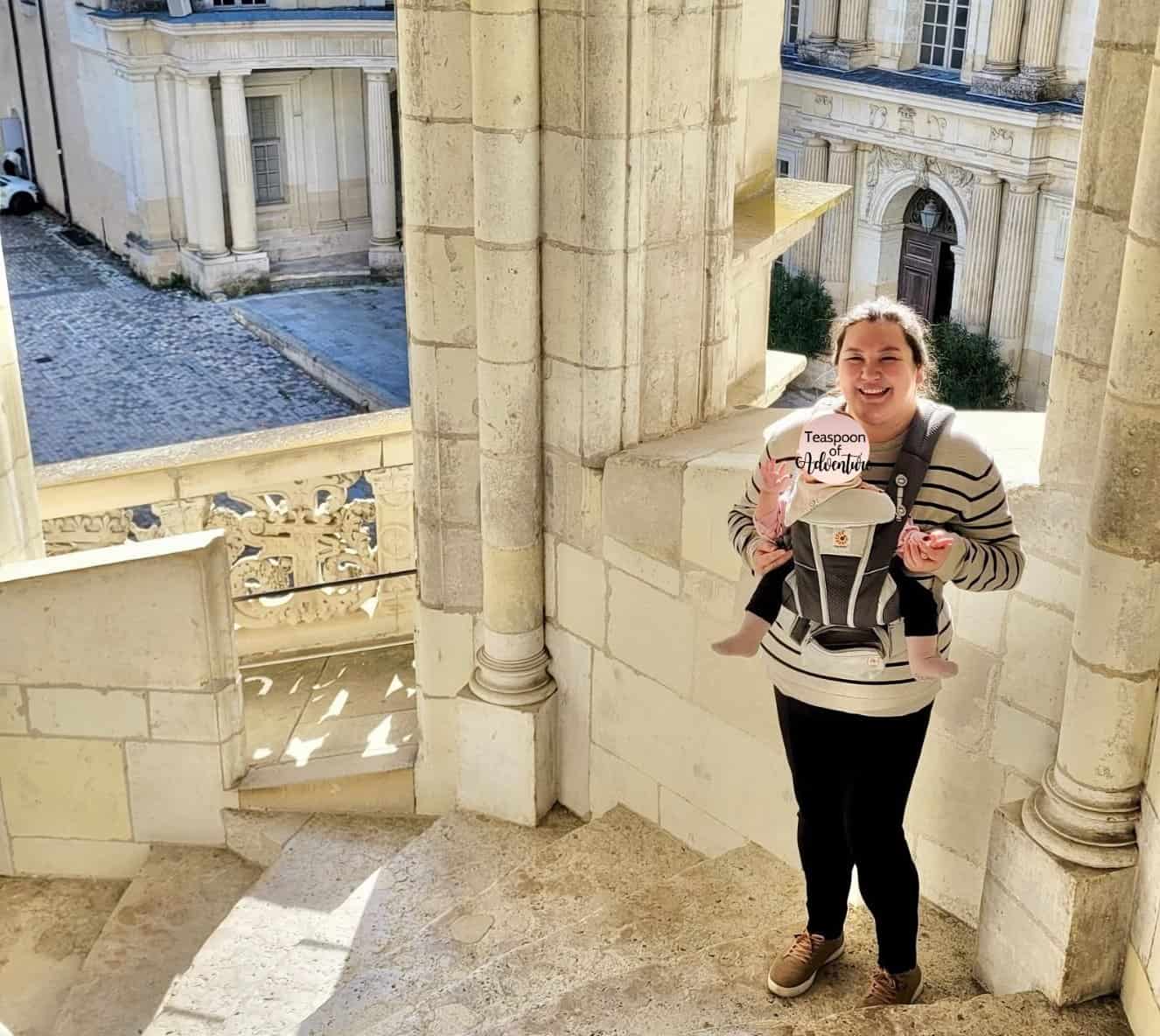 Tips for Flying With a Baby: From Booking to Baggage Claim 15 Riana Ang-Canning, travel blogger at Teaspoon of Adventure, stands on the steps of an external stairwell at Blois Castle, France, wearing her daughter in a carrier on her chest