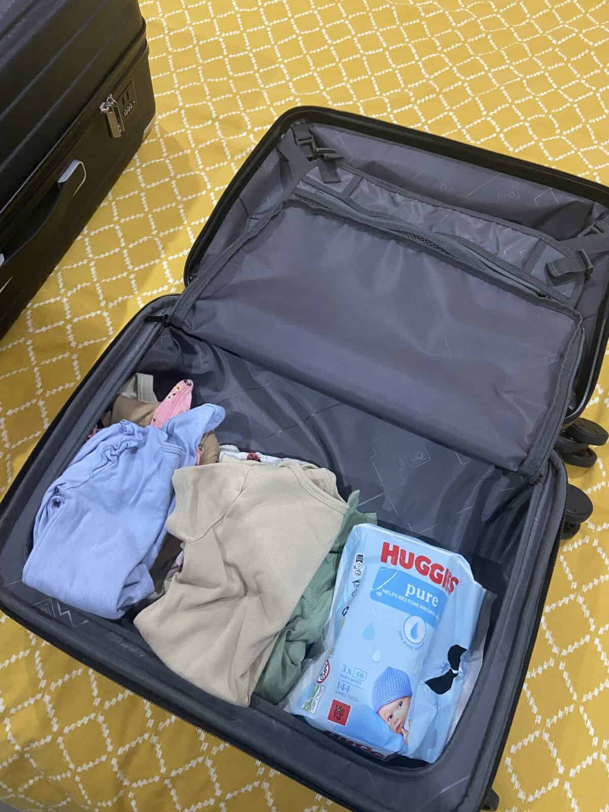 Our Essential Packing List for Travel with a Baby 21 Baby onesies and Huggies wipes packed into the LEVEL8 Grace hardside carry-on suitcase