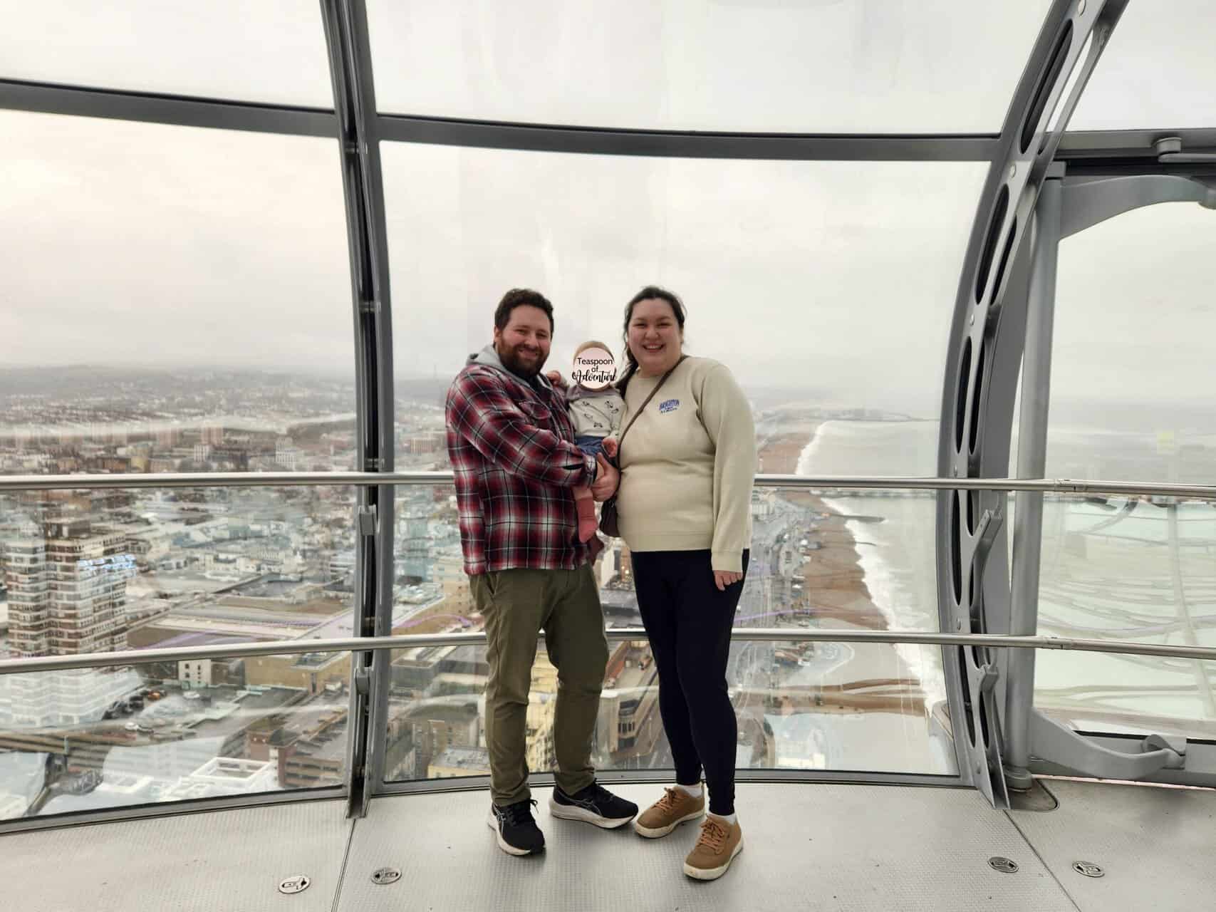 Colin, Riana and Baby C posing inside the Brighton i360 glass pod elevator with the views of Brighton and the English Channel behind them