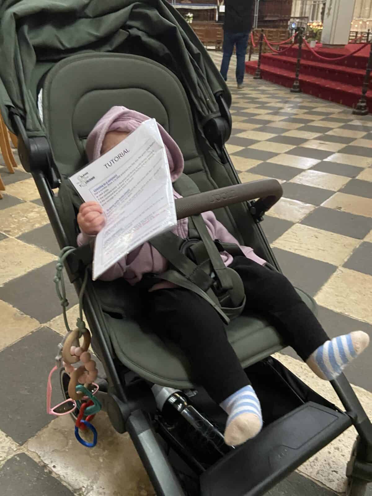 Joolz Aer Review: Is This the Best Travel Stroller? 3 Baby C in her Joolz Aer+ travel stroller inside the Orleans Cathedral holding a piece of paper
