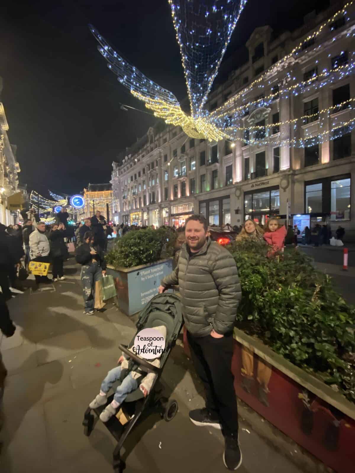20+ Things to Do in London With a Baby 42 Colin standing behind Baby C in her stroller under a Christmas lights display in London, England