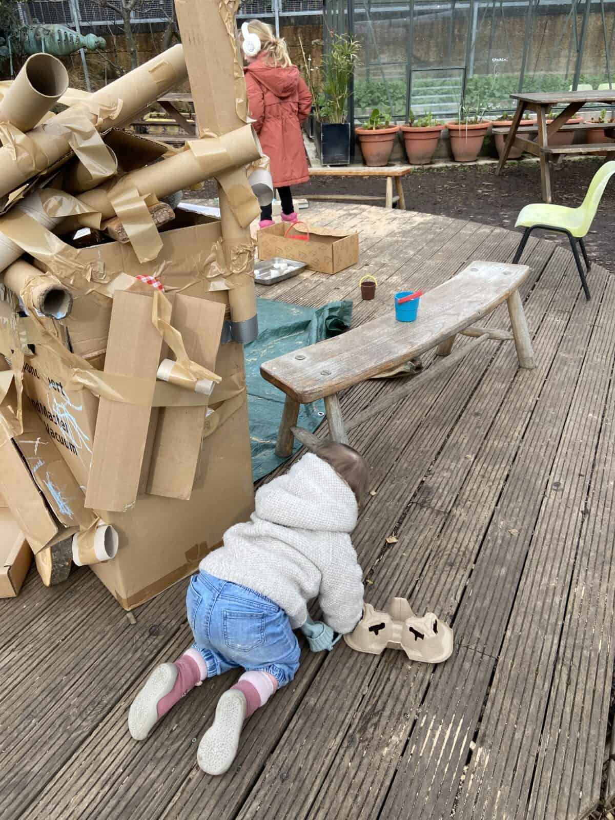 20+ Things to Do in London With a Baby 46 Baby C crawling around a wooden platform at Spitalfields City Farm in London with a large cardboard structure on it