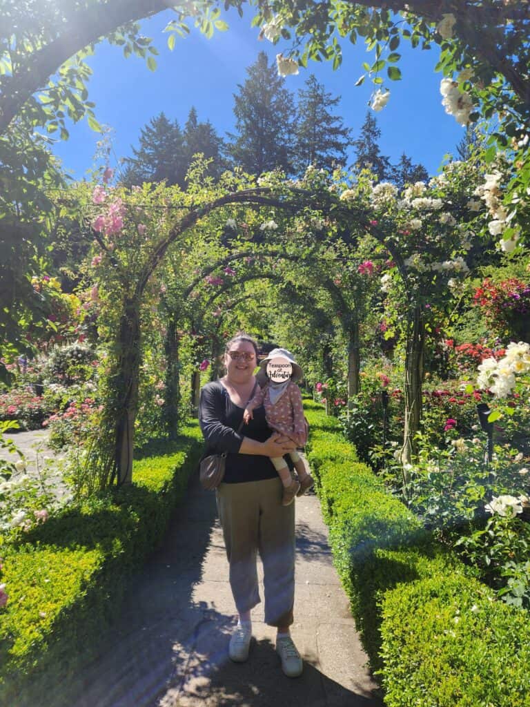 Riana and Baby C standing in the Rose Garden under arches of greenery and flowers in Butchart Gardens, Victoria, BC