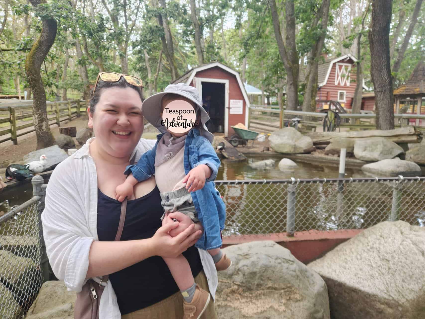 Riana holds Baby C in front of the duck pond at Beacon Hill Petting Zoo and Children's Farm in Beacon Hill Park in Victoria, BC