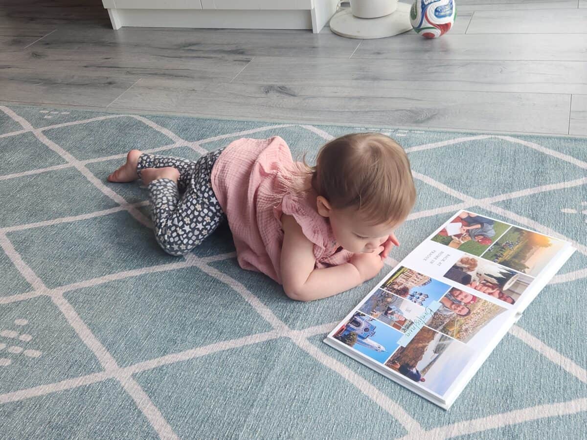 Making A Custom Board Book From Our Travel Photos 12 Baby C lying on the carpet flipping through a family photo book