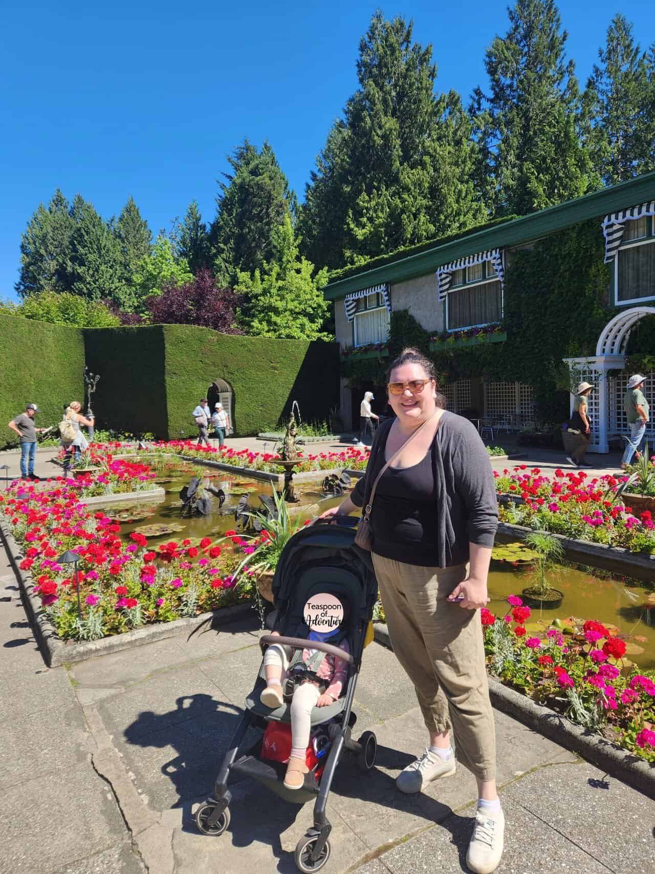 Riana and Baby C in her stroller in front of the Italian Garden water feature and flowers at The Butchart Gardens