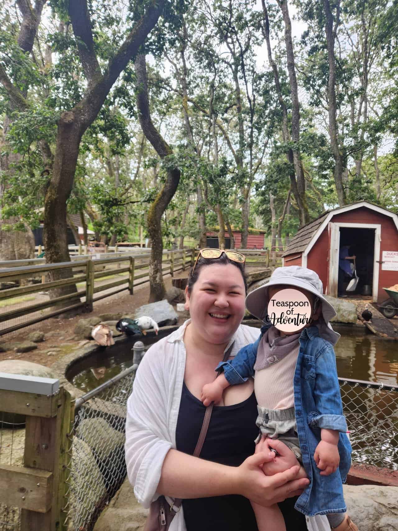 Riana holds Baby C in front of the duck pond at Beacon Hill Petting Zoo and Children's Farm in Beacon Hill Park in Victoria, BC
