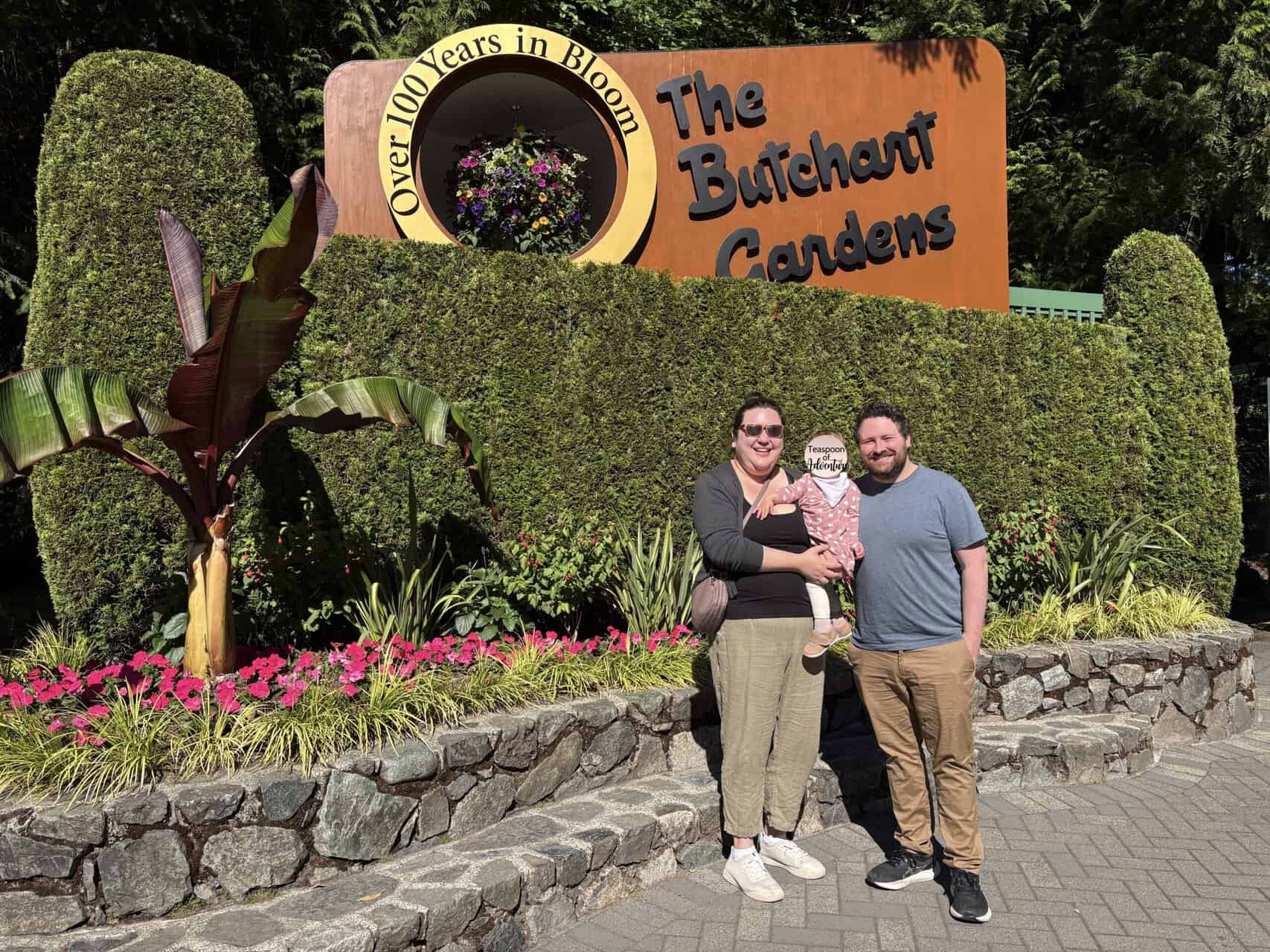 Riana, Colin and Baby C posing in front of The Butchart Gardens entrance sign