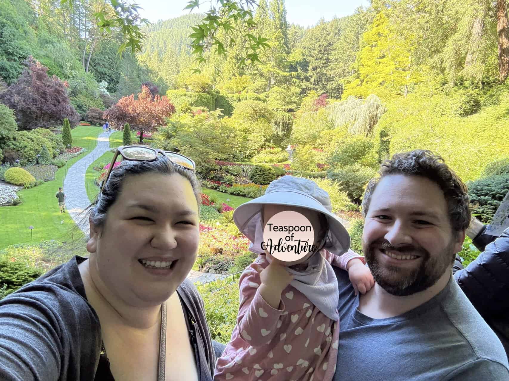 How to Get to Victoria from Vancouver, BC 18 Selfie of RIana, Colin and Baby C smiling in front of the Sunken Garden in Butchart Gardens, Victoria