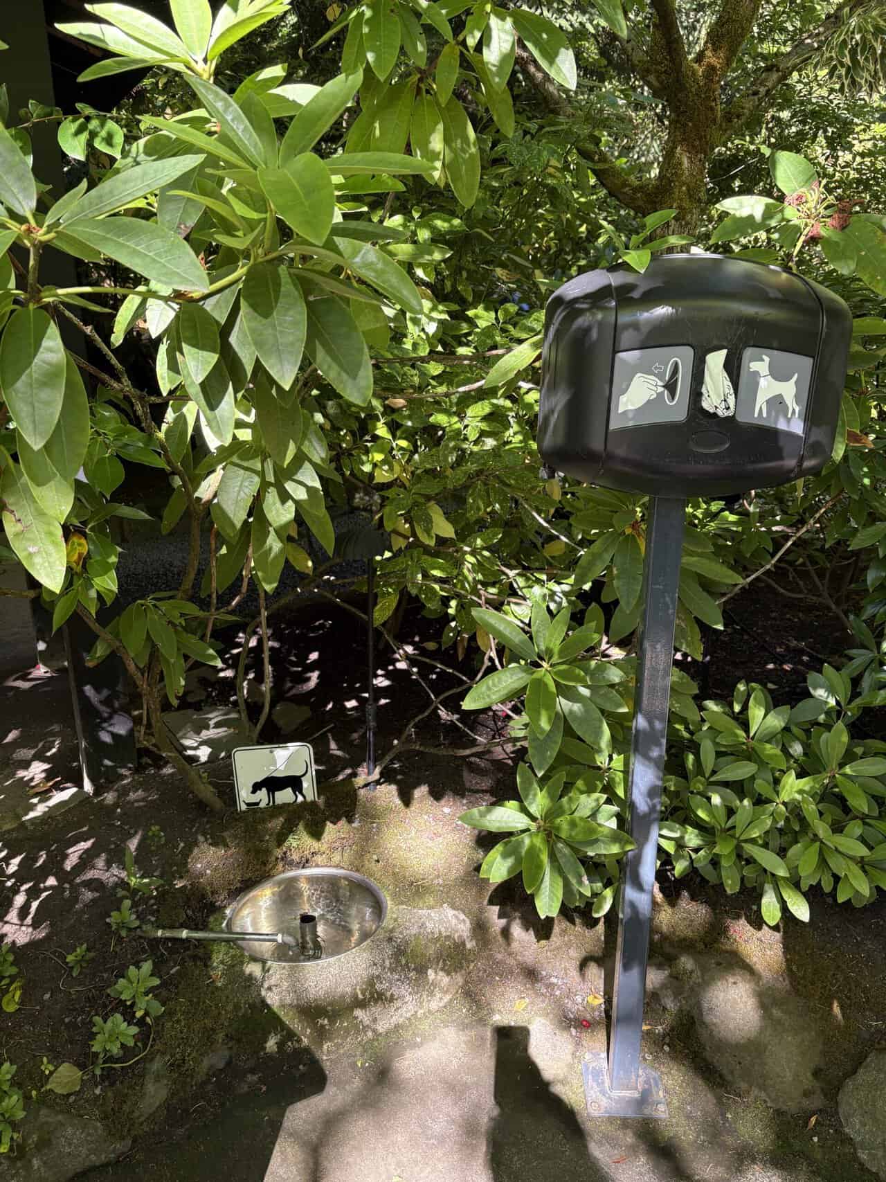 A post with dog bags, a dog water bowl and a little sign showing how dog-friendly The Butchart Gardens are 