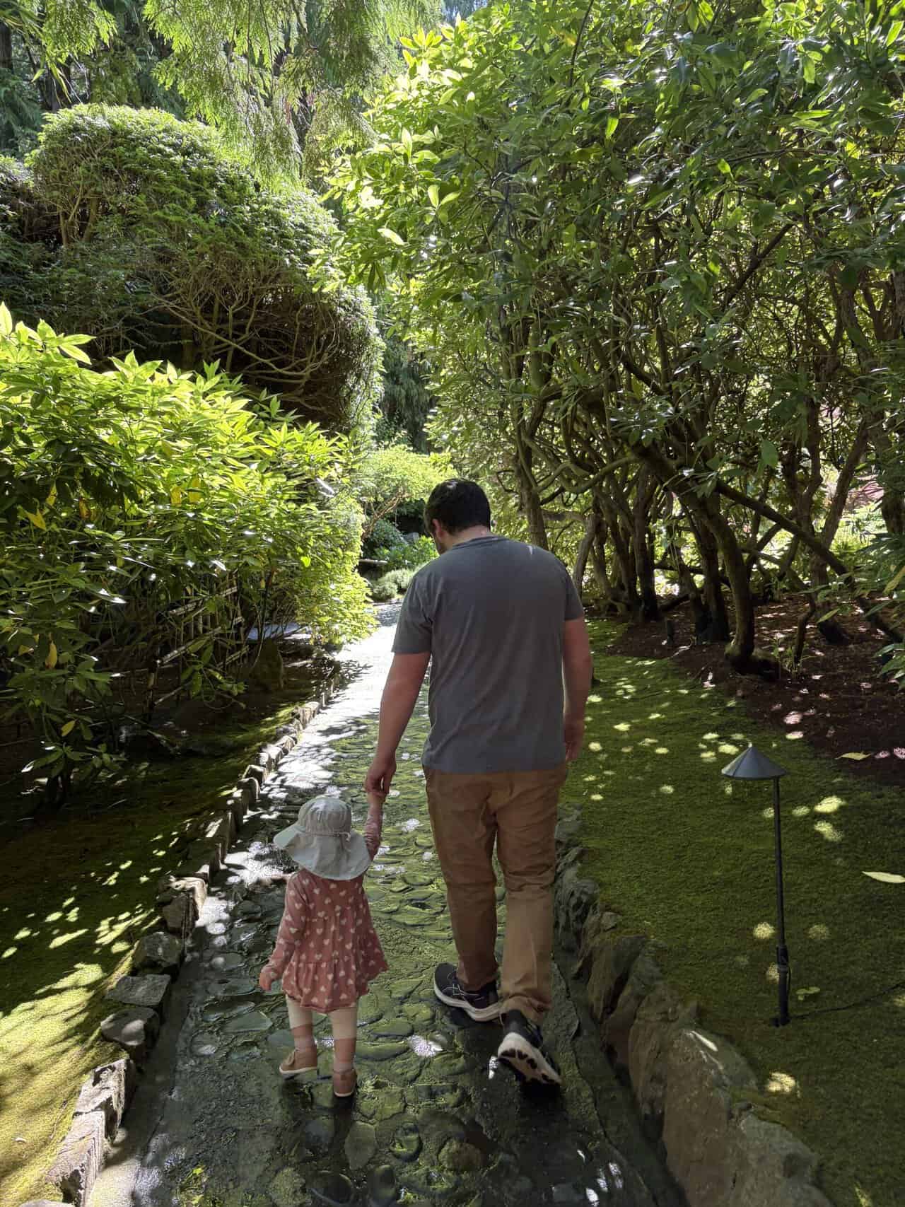 Colin and Baby C walking down a pathway with trees and hedges at The Butchart Gardens