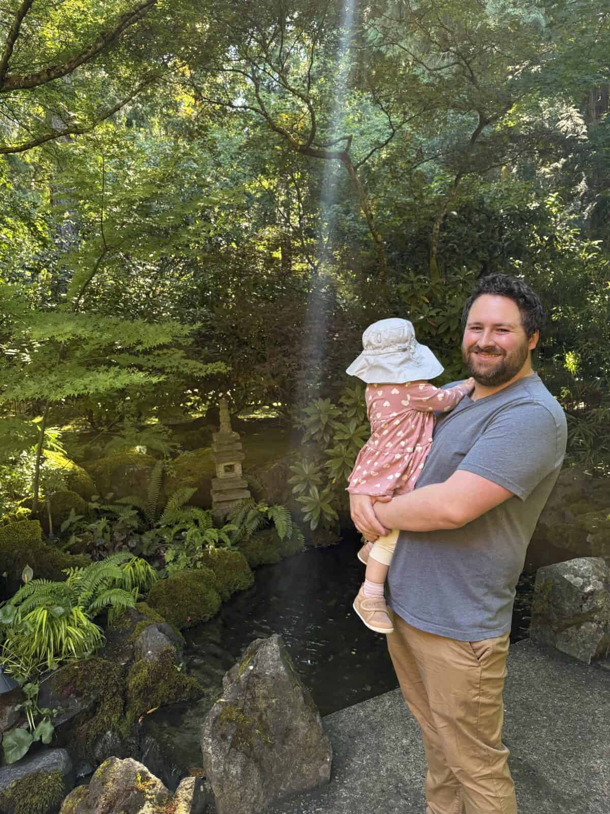 Colin holding Baby C in front of a small pond at Butchart Gardens