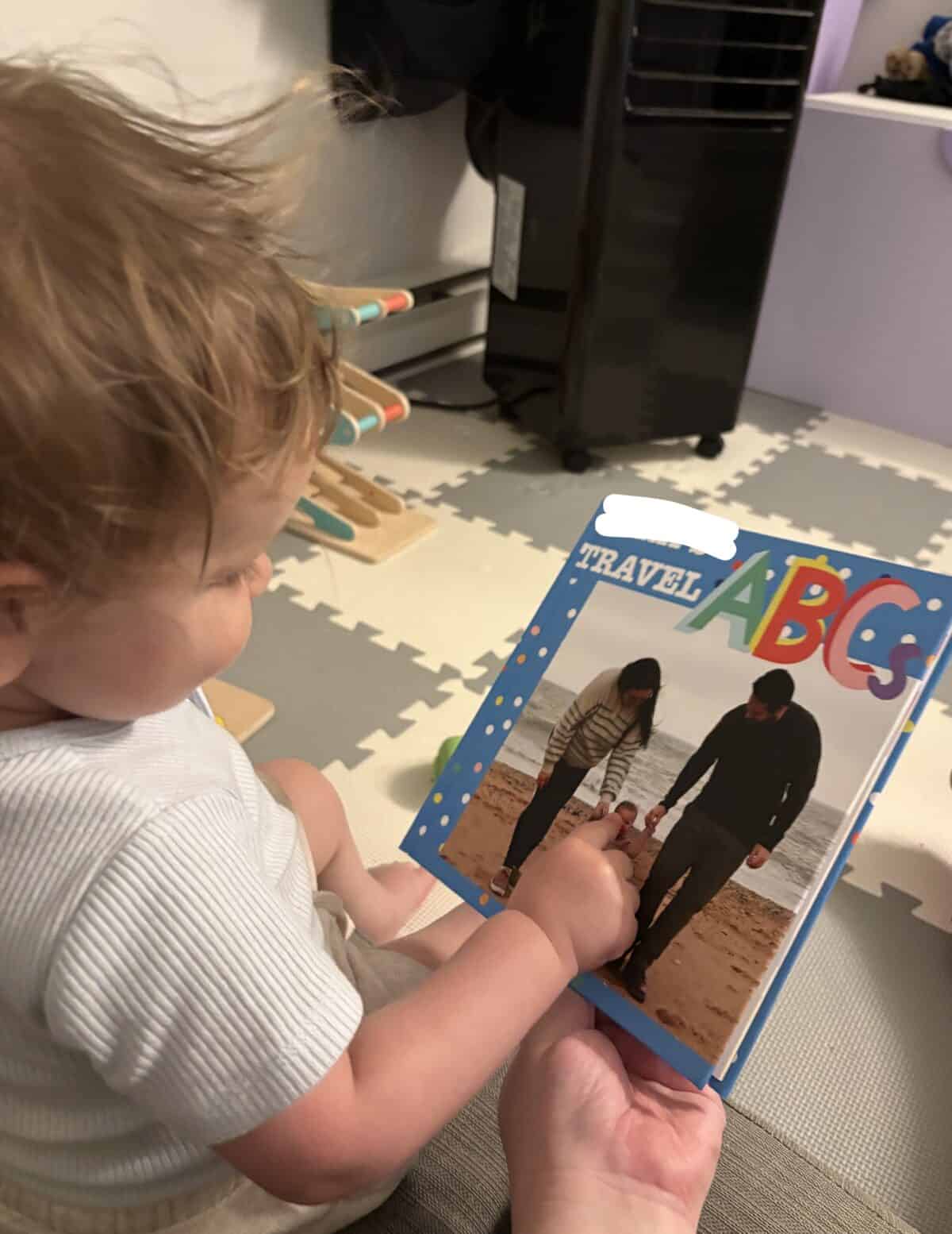 Making A Custom Board Book From Our Travel Photos 10 C pointing to the front of her custom Mixbook that says Travel ABCs with a family photo
