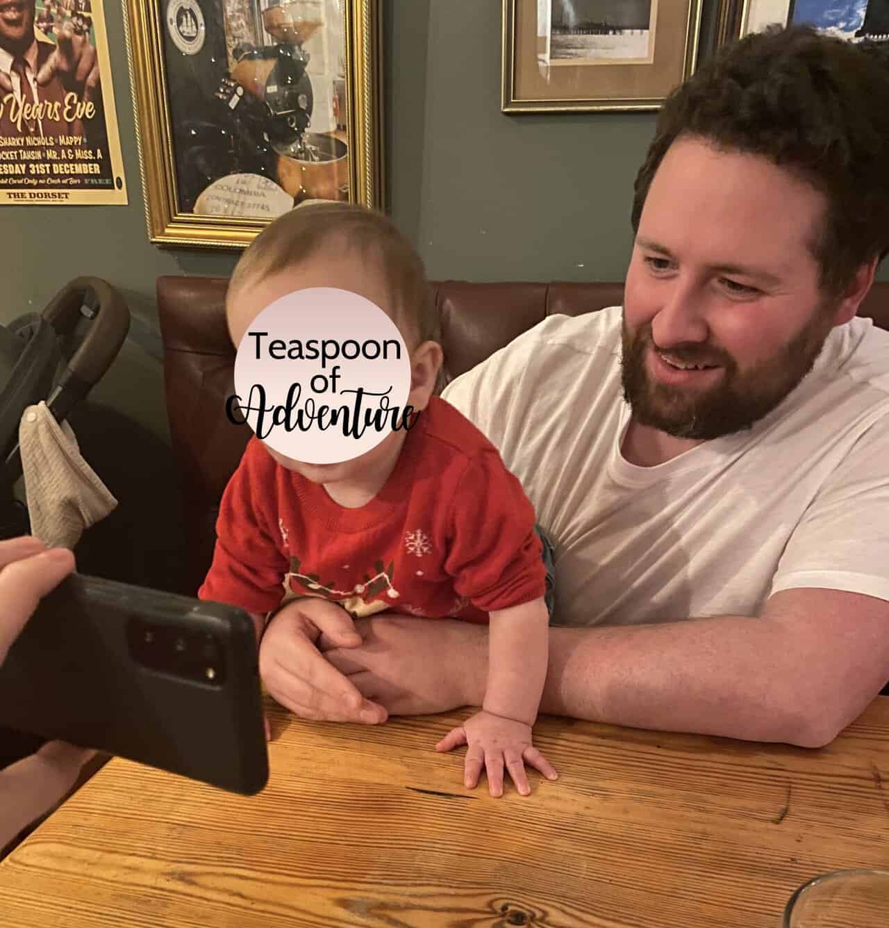 Why an eSIM Is Essential for Family Travel 2 Colin holding Baby C at a restaurant booth. They're both looking at a phone screen Riana is holding out to them.