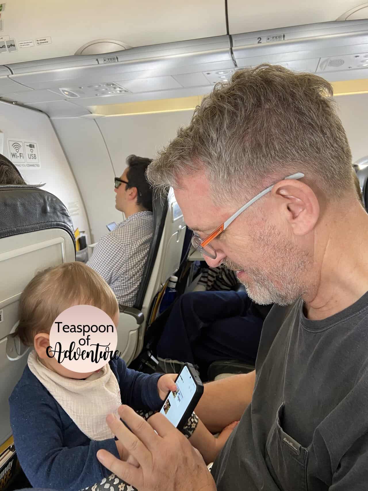 Why an eSIM Is Essential for Family Travel 4 Riana's father sitting on an airplane with Baby C on his lap. Baby C is scrolling on his phone.