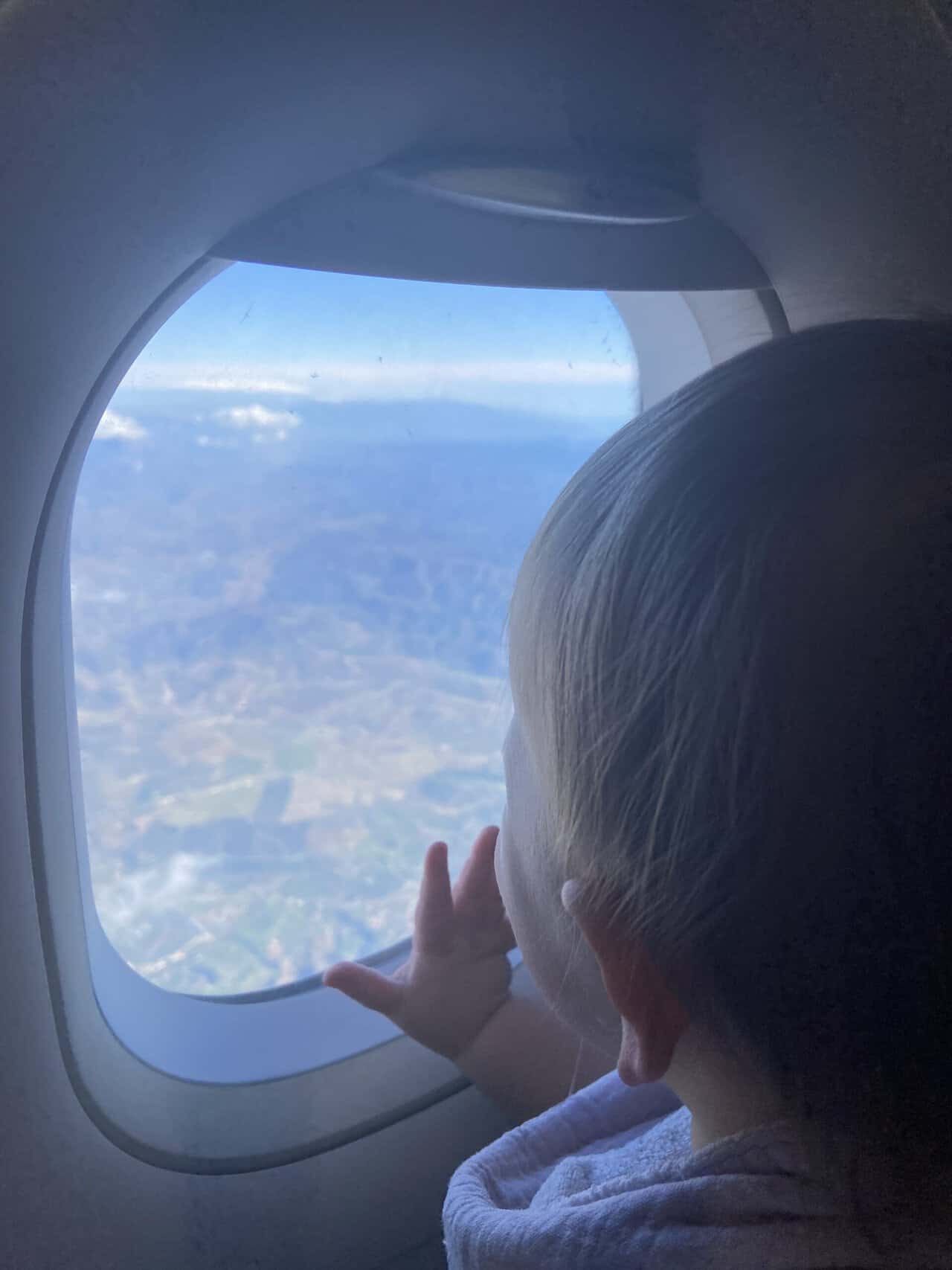 Tips for Flying With a Baby: From Booking to Baggage Claim 3 Baby C looking out the plane window with her hand on it