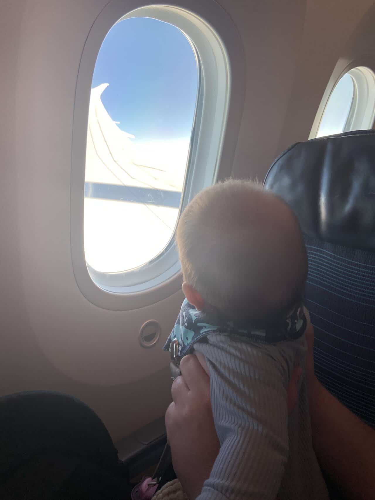 Tips for Flying With a Baby: From Booking to Baggage Claim 4 Baby C looking out the plane window at clouds and the wing on baby's first flight