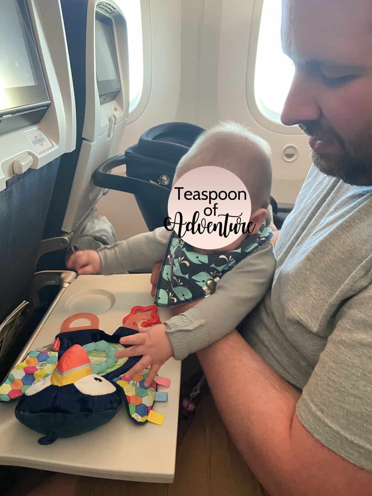 Tips for Flying With a Baby: From Booking to Baggage Claim 22 Baby C playing with toys on the tray table while sitting on Colin's lap during her first flight
