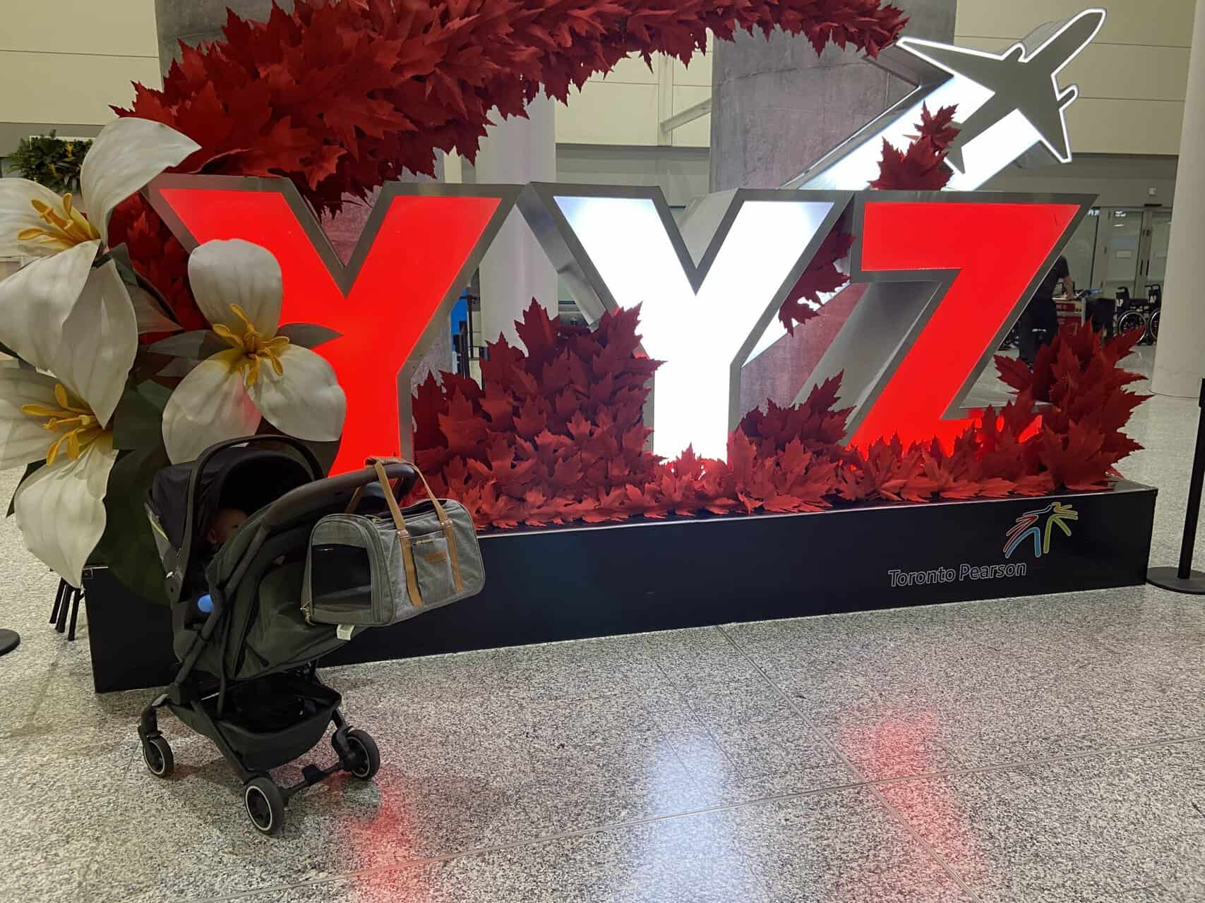 Tips for Flying With a Baby: From Booking to Baggage Claim 48 Baby C in her stroller in front of a YYZ sign at Toronto Airport