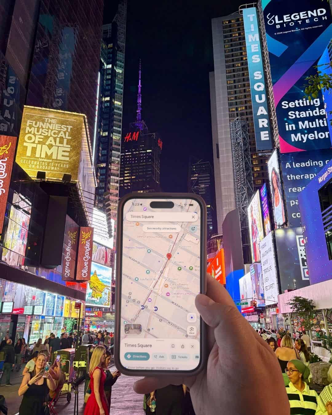 Riana holding up her phone with Google Maps open on it in Times Square, Manhattan, New York City