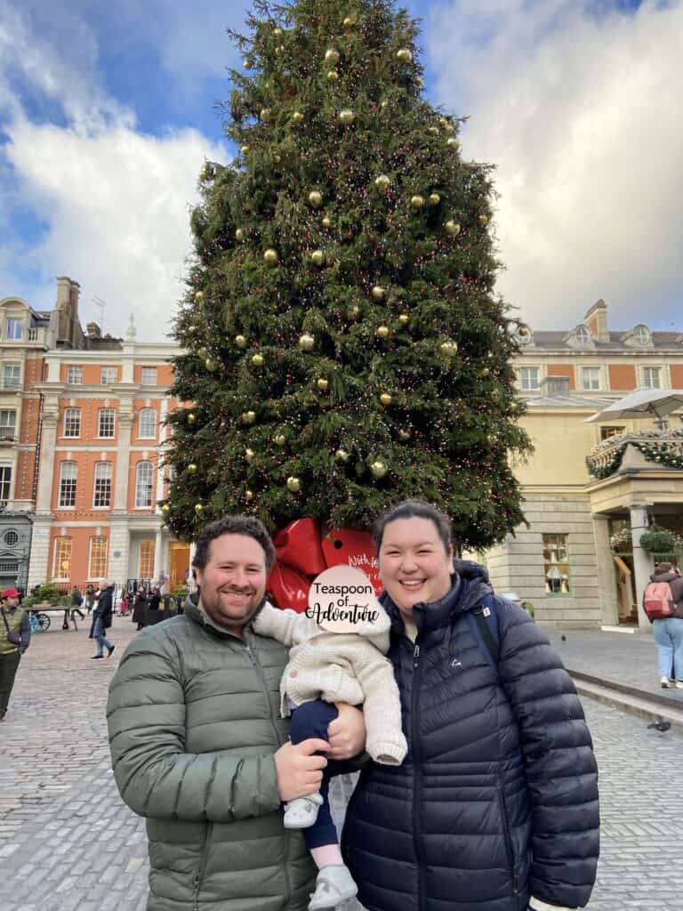 Colin and Riana holding C in front of a Christmas tree at Covent Garden, London, UK in the winter in Europe