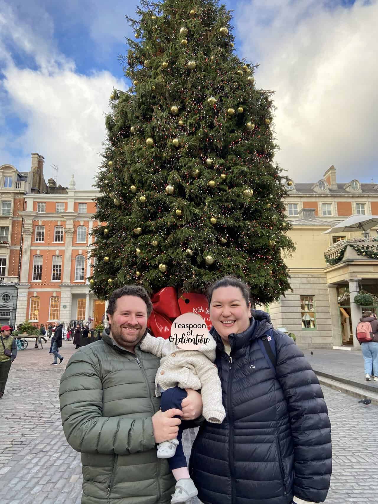 Colin and Riana holding C in front of a Christmas tree at Covent Garden, London, UK in the winter in Europe